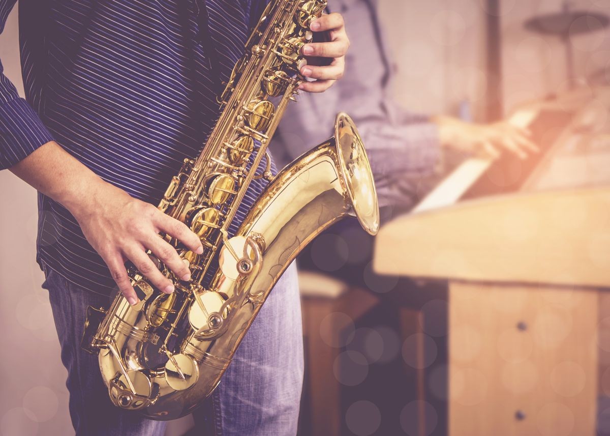 young musician man plays tenor saxophone on stage with pianist with light bobkeh effected over blurred music instrument background