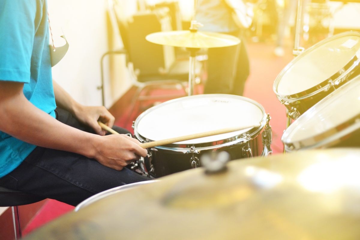 The man is playing drum set in low light background.